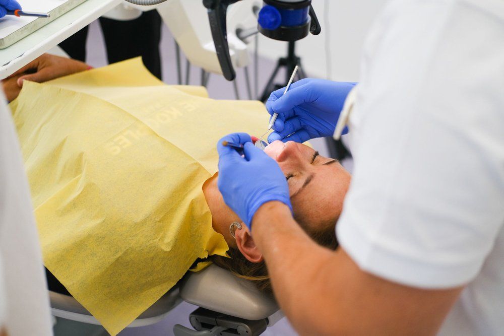 A woman is laying in a dental chair while a dentist examines her teeth.