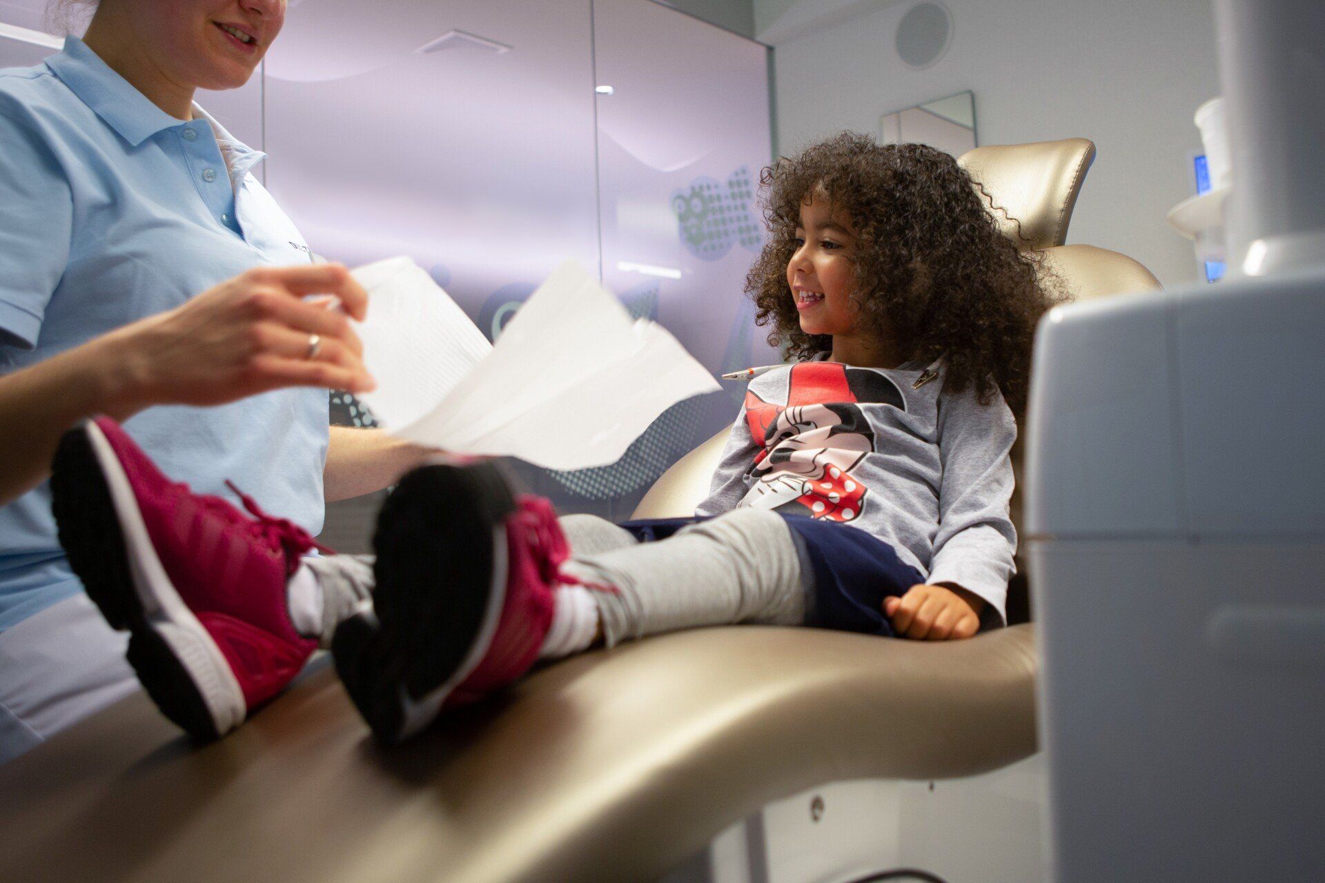 A little girl is sitting in a dental chair talking to a dentist.