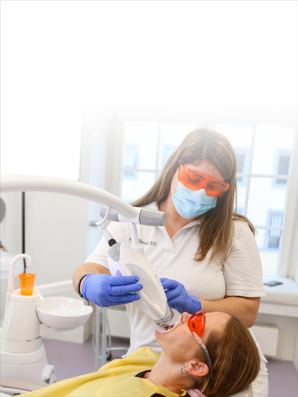 A woman is getting her teeth whitened by a dentist in a dental office.