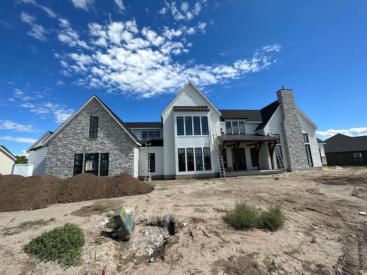 Back view of a large white house with stone accents, under construction, blue sky with clouds.