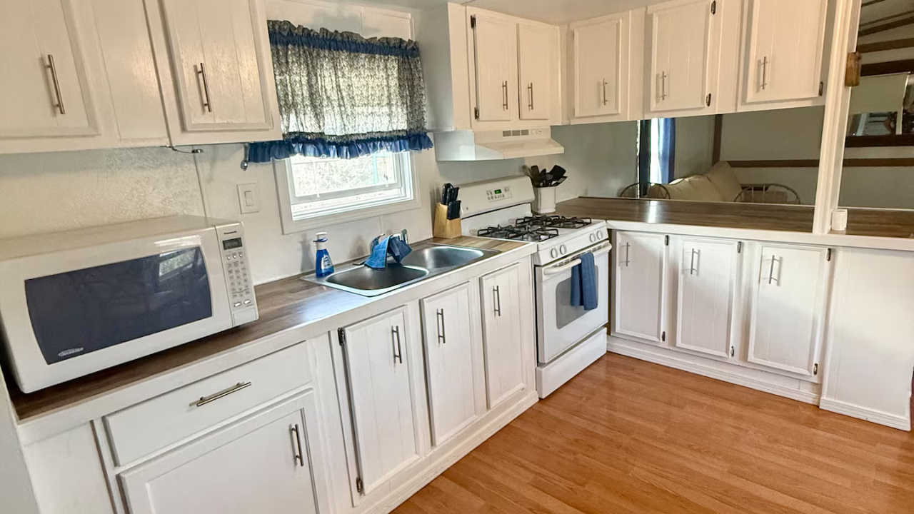 White kitchen with upper and lower cabinets, microwave, stove, and sink.