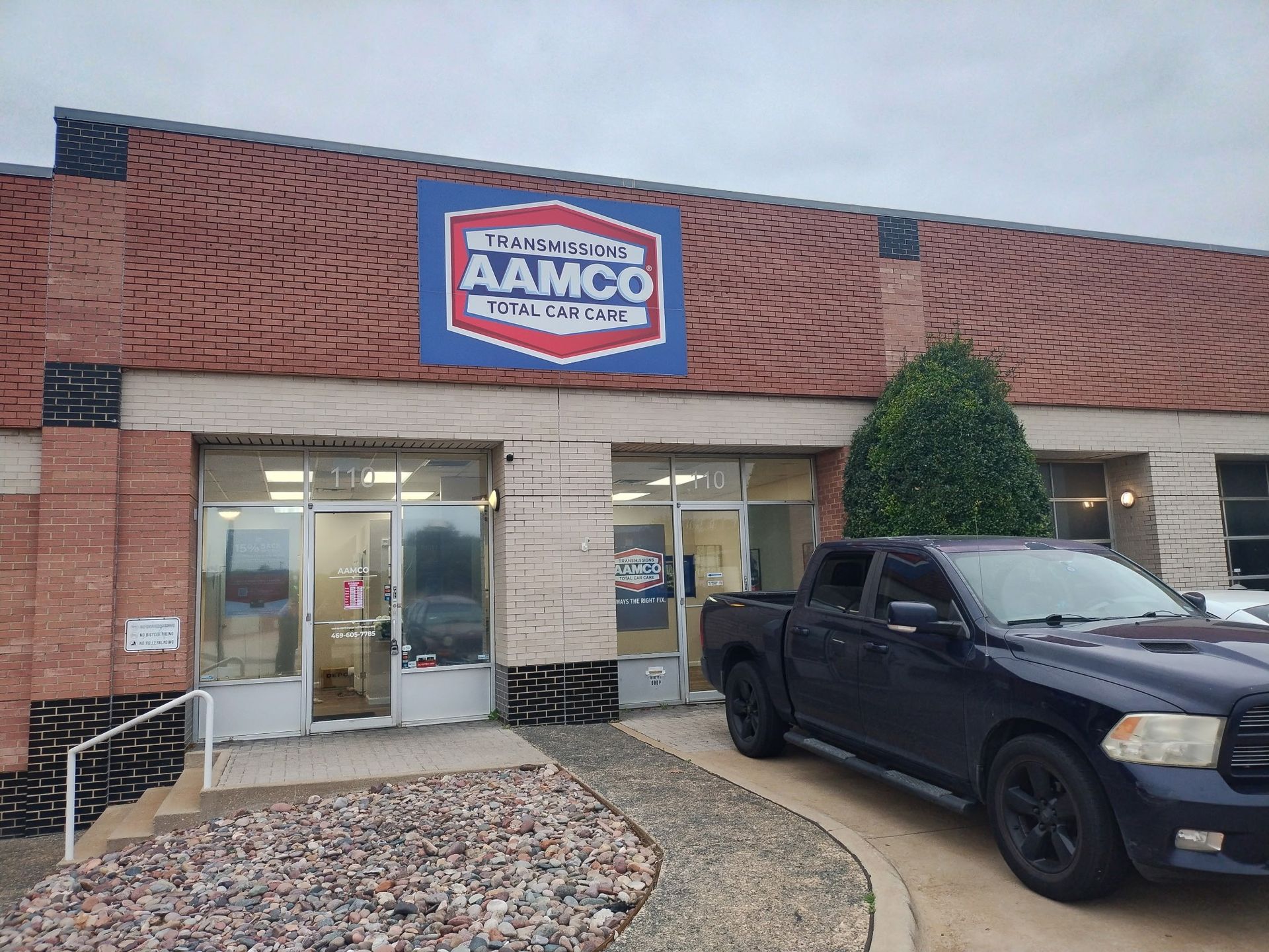 AAMCO Carrollton, TX - Transmission and auto repair shop exterior with brick facade and a black pickup truck parked outside