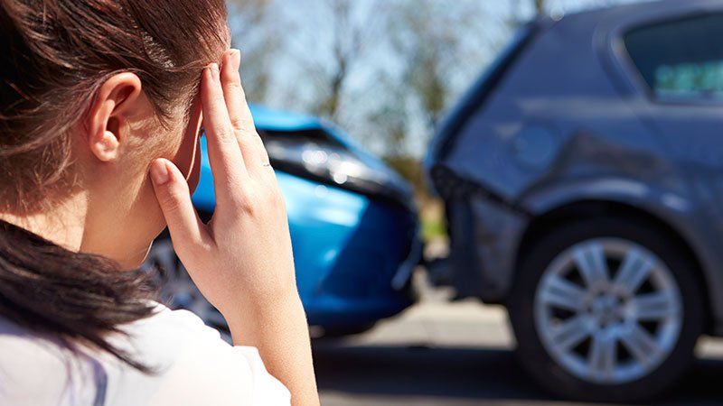Distressed woman looking at the aftermath of a rear ended car
