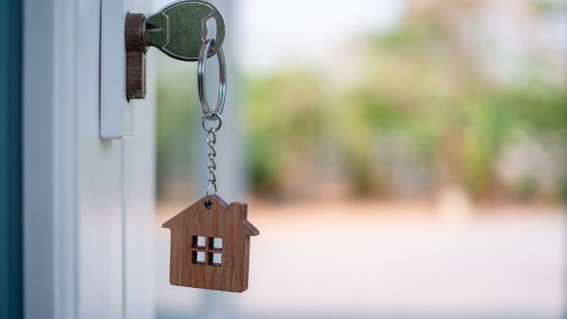 Key with house-shaped keychain in a door's keyhole, suggesting home access.