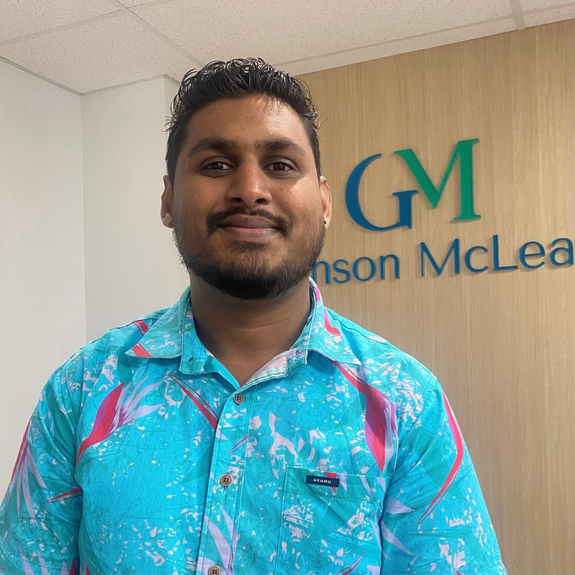 Man in turquoise patterned shirt smiles in front of a 