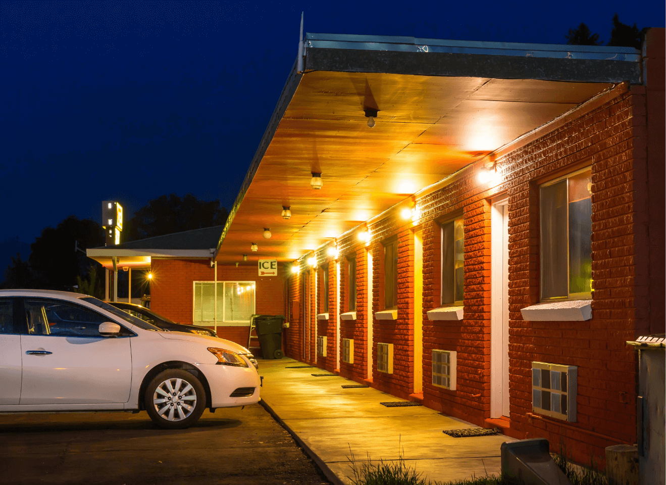 Red brick motel lit up at night, with a white car parked outside.