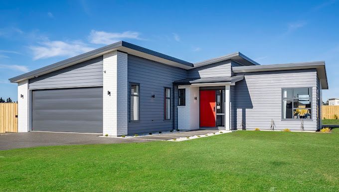 Modern gray house with red door and attached garage under a blue sky.