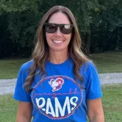 Woman in sunglasses wearing a blue Rams T-shirt and smiling outdoors.