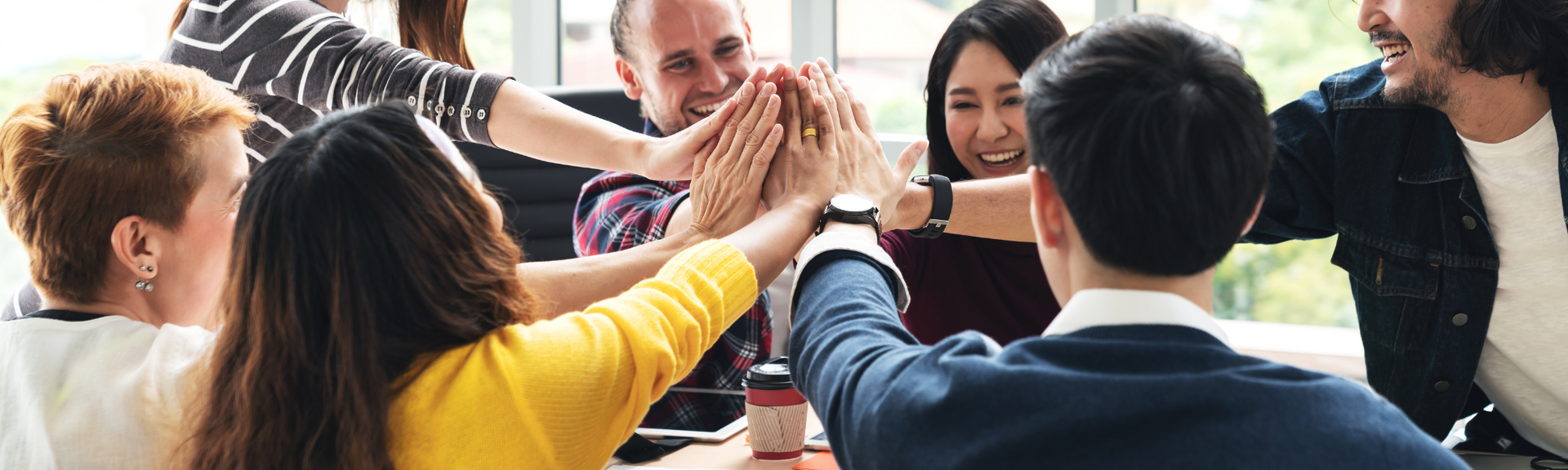 Group of coworkers stacking hands in a bright office, celebrating teamwork and collaboration