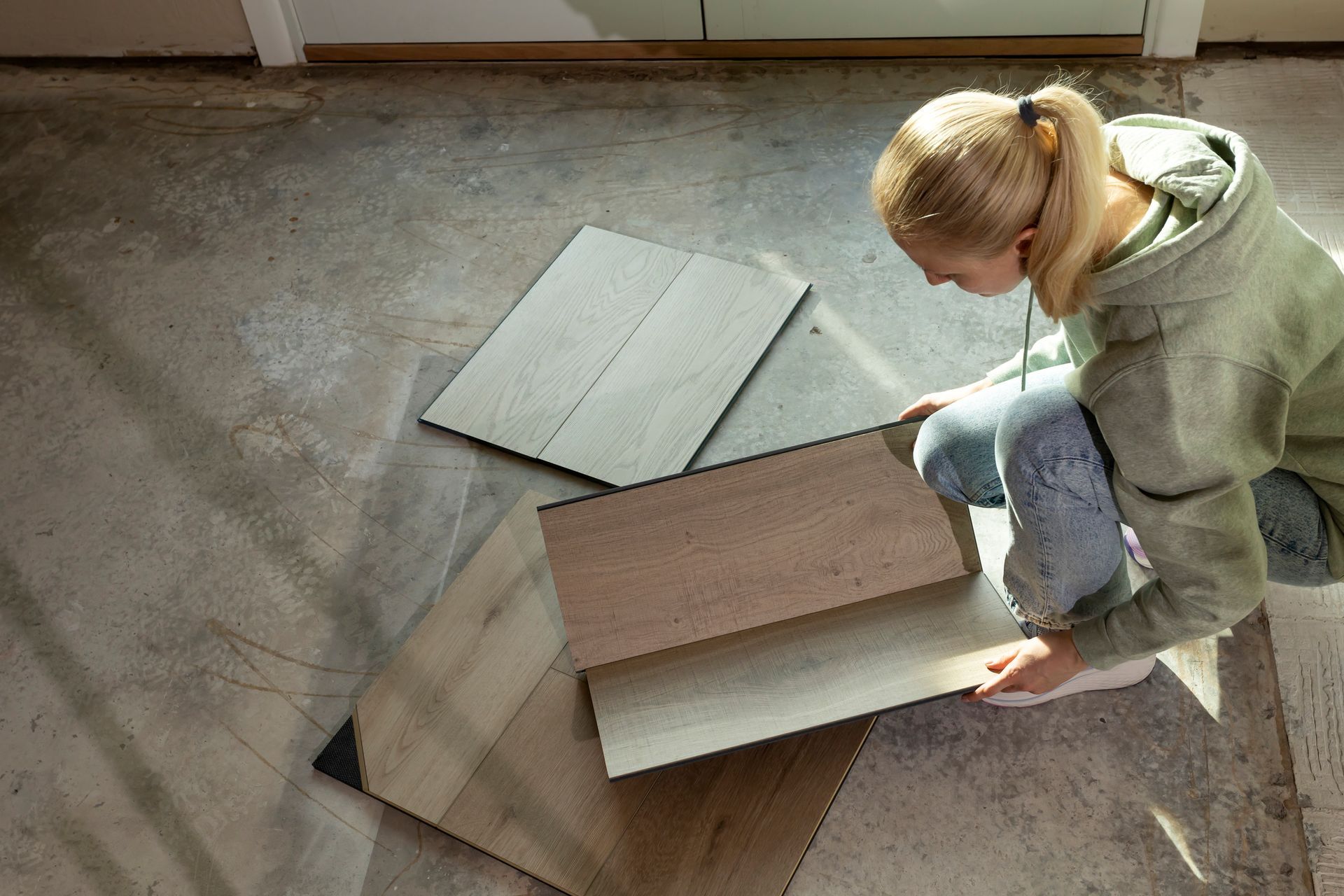 Woman holding luxury vinyl wood samples on a concrete floor, selecting waterproof flooring options