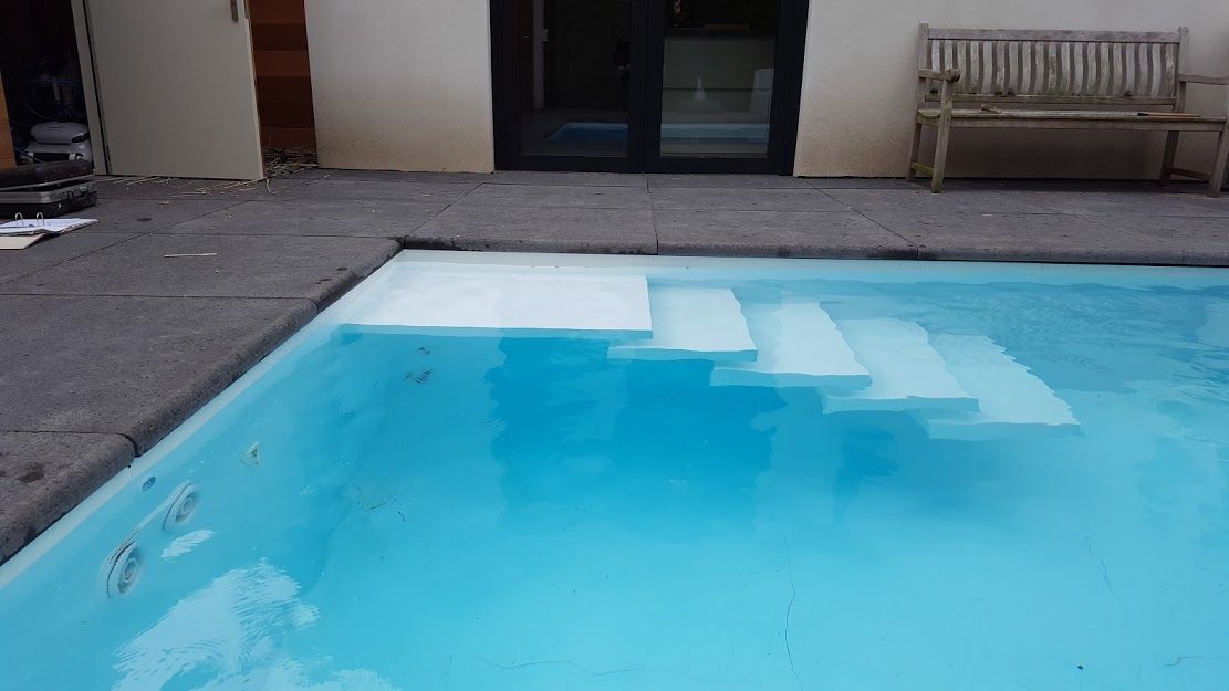Zwembad (PanelPool) met witte trappen en blauw water, omzoomd door donkergrijze stenen en een licht gebouw.
