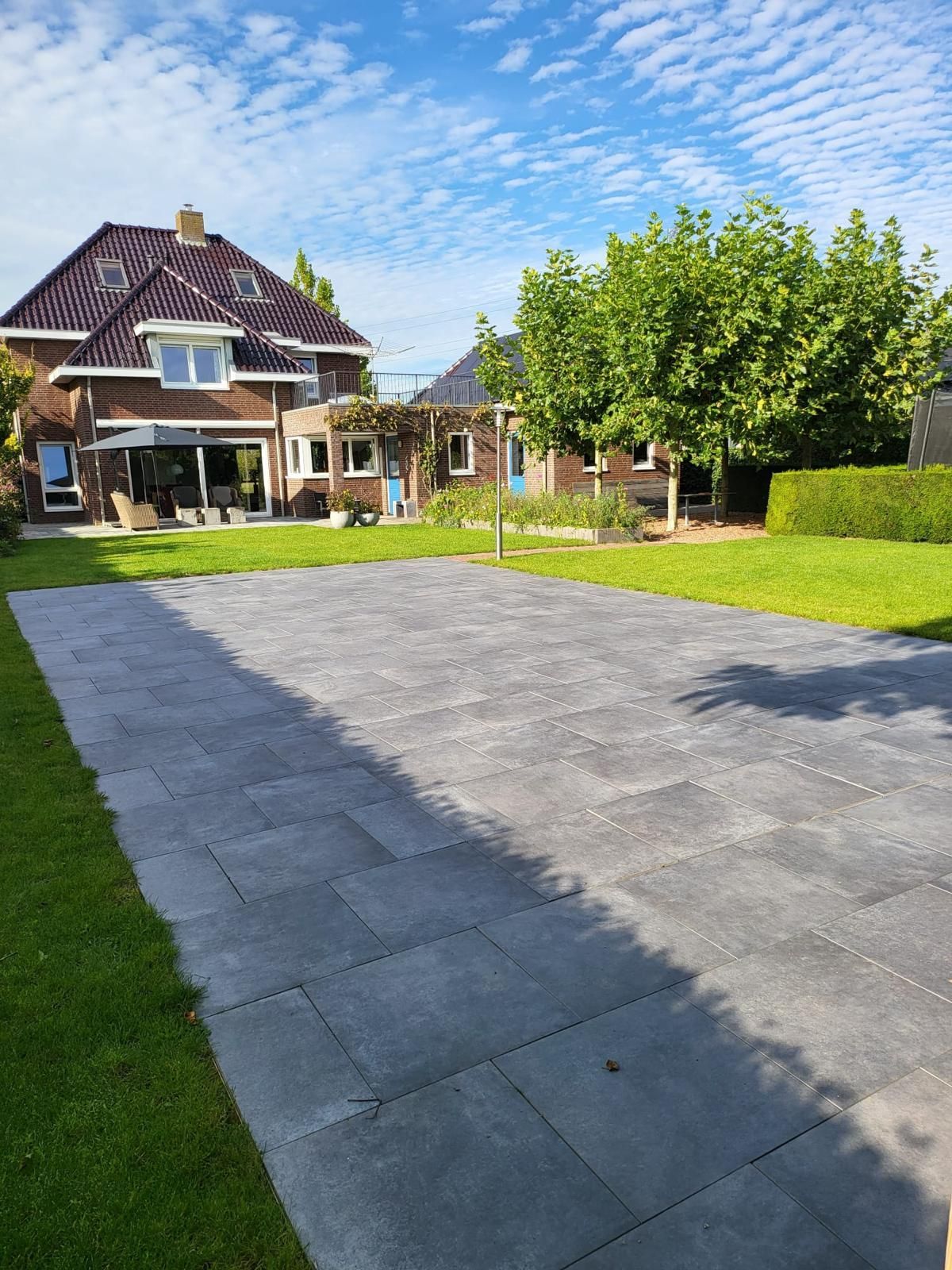 Een grijs stenen terras in een zonnige achtertuin met een groot huis en een MagicPool