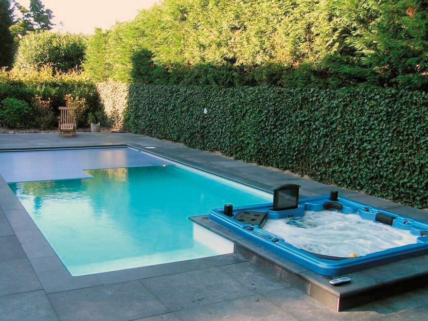 Zwembad met aangebouwde jacuzzi, gelegen in een achtertuin. grijs stenen terras. PanelPool