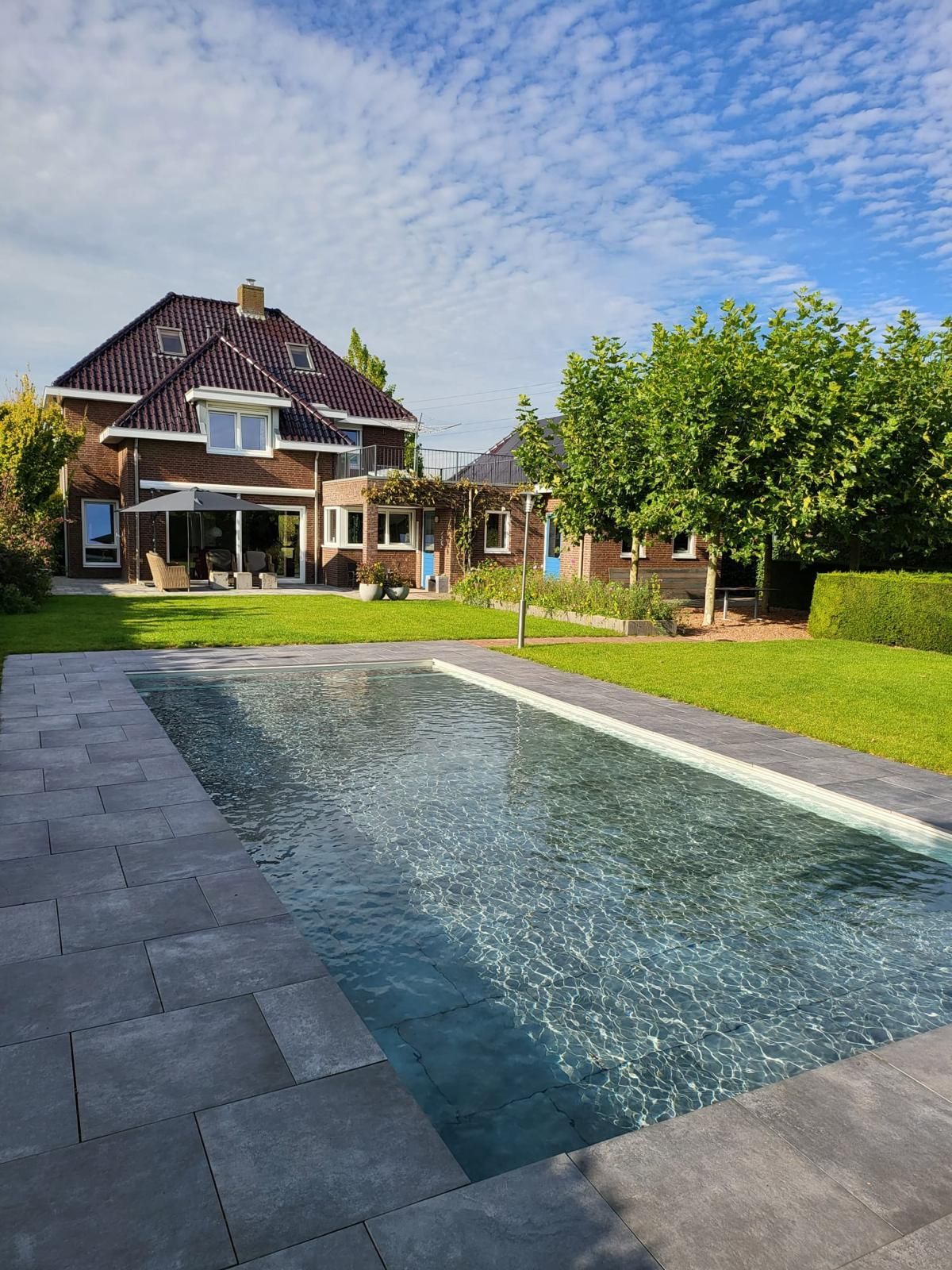 Een achtertuin met een MagicPool, gazon en een bakstenen huis onder een blauwe hemel.