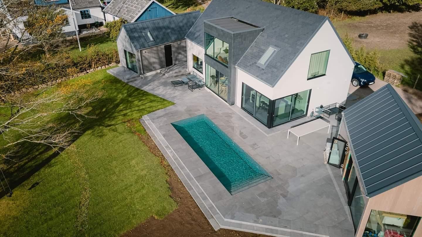 Moderne woning met een rechthoekig MagicPool, een grijs dak en een omringend groen gazon.