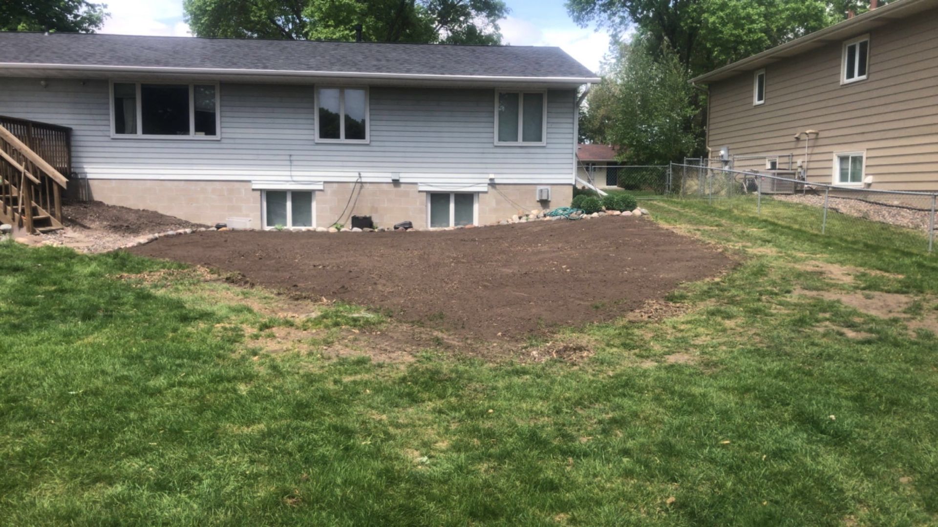 Backyard with a large freshly spread dirt mound behind a gray house and grassy lawn
