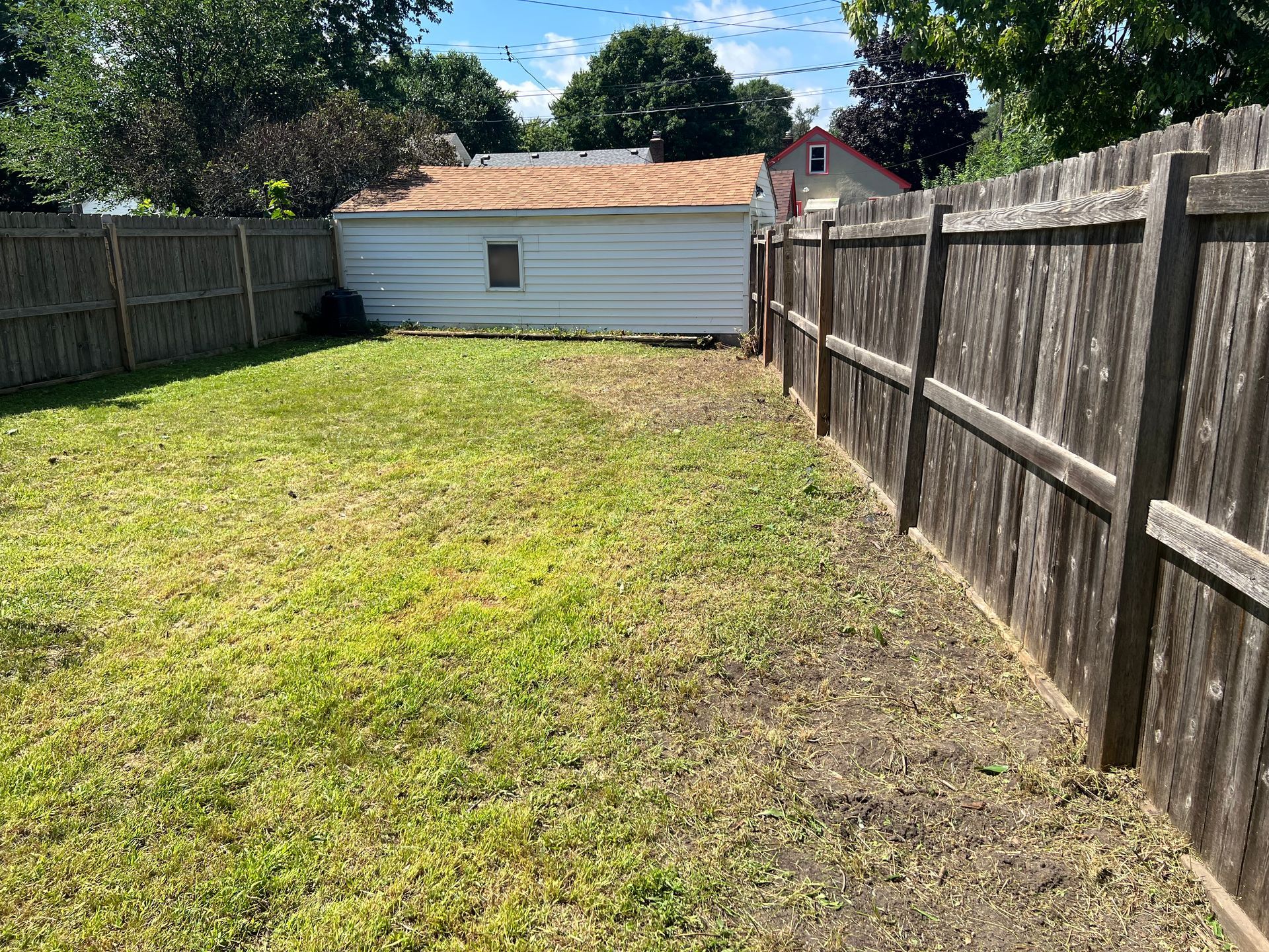 Narrow grassy backyard with wooden fences and a small white shed at the far end.