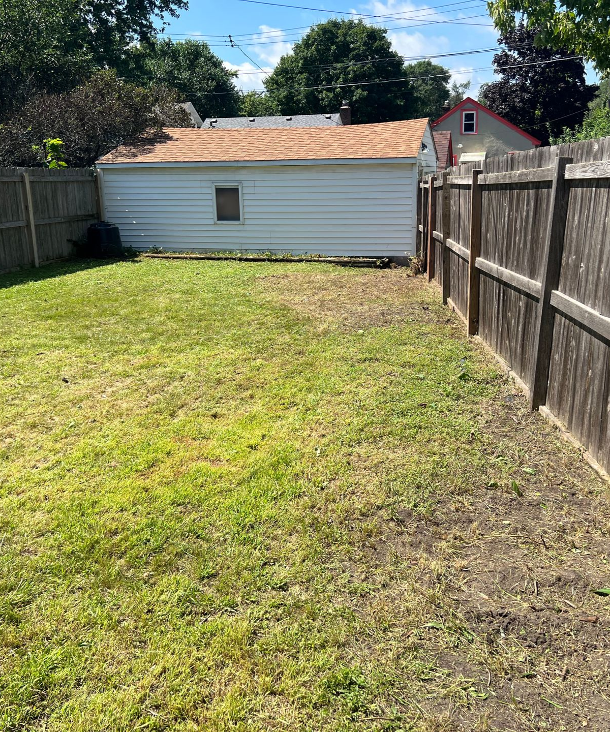 Small fenced backyard with grass, wooden privacy fences, and a white shed in the background.