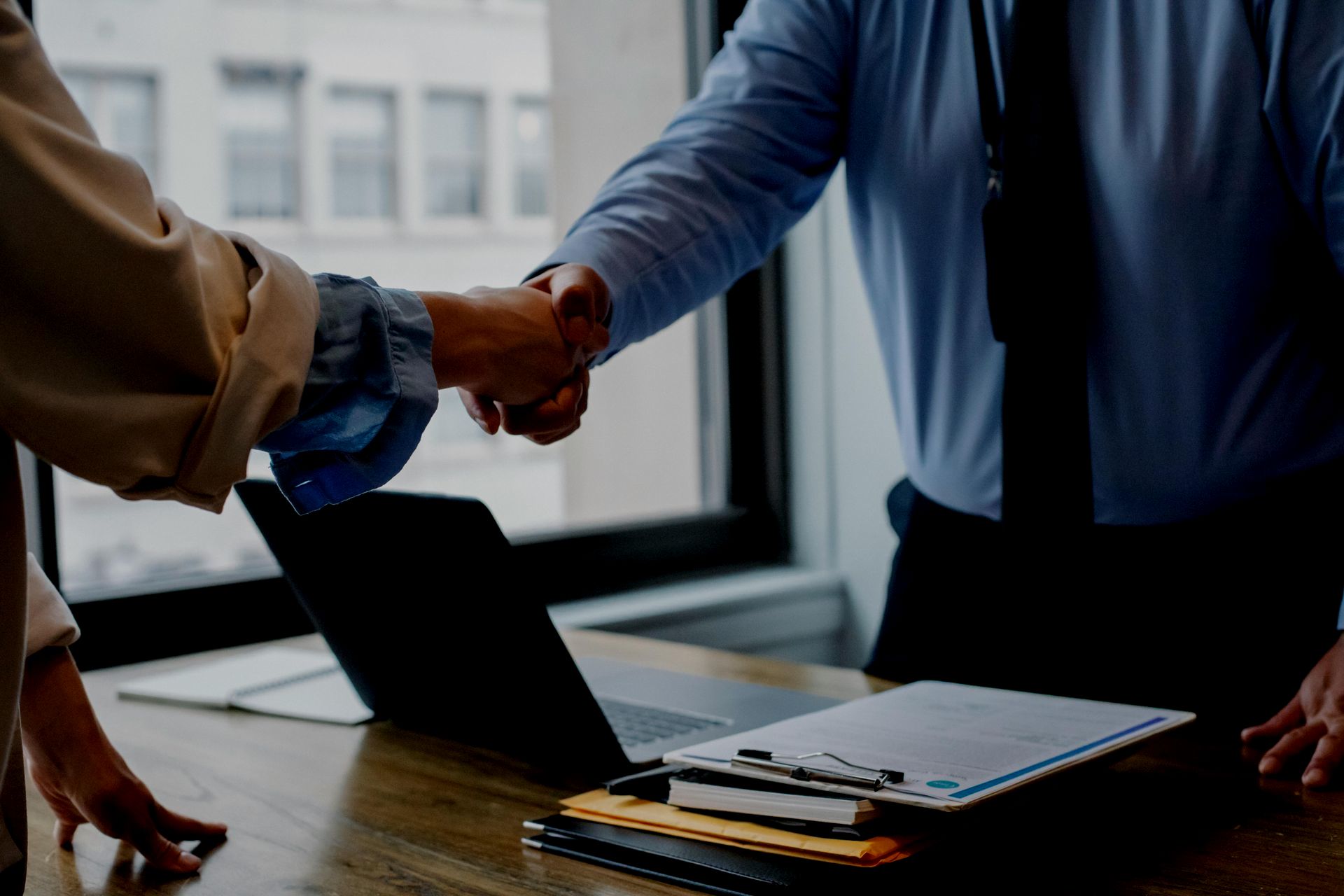 A man and a woman are shaking hands in front of a laptop.