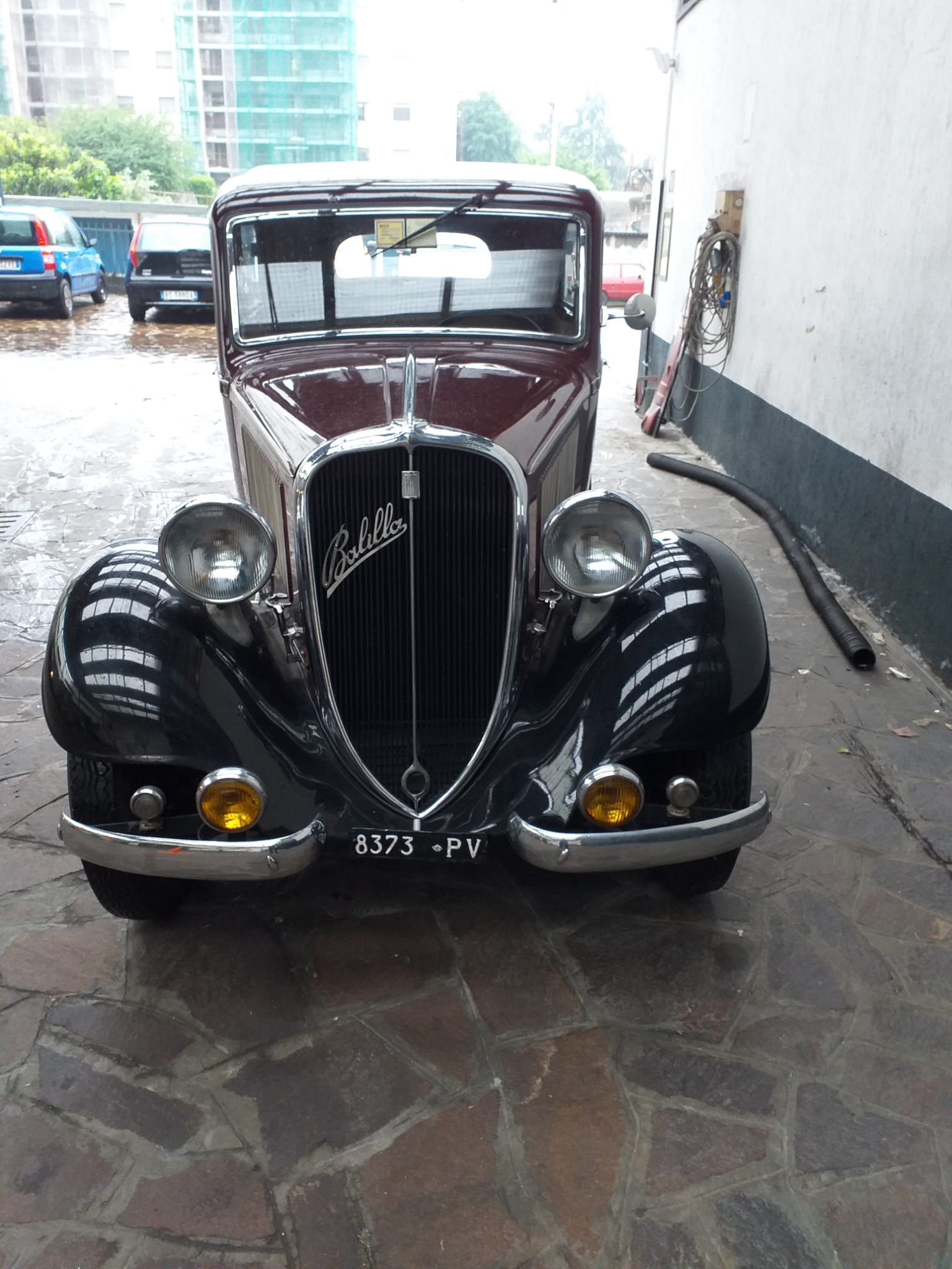 Vista frontale di un'auto nera d'epoca con parafanghi arrotondati, parcheggiata in uno stretto vicolo.
