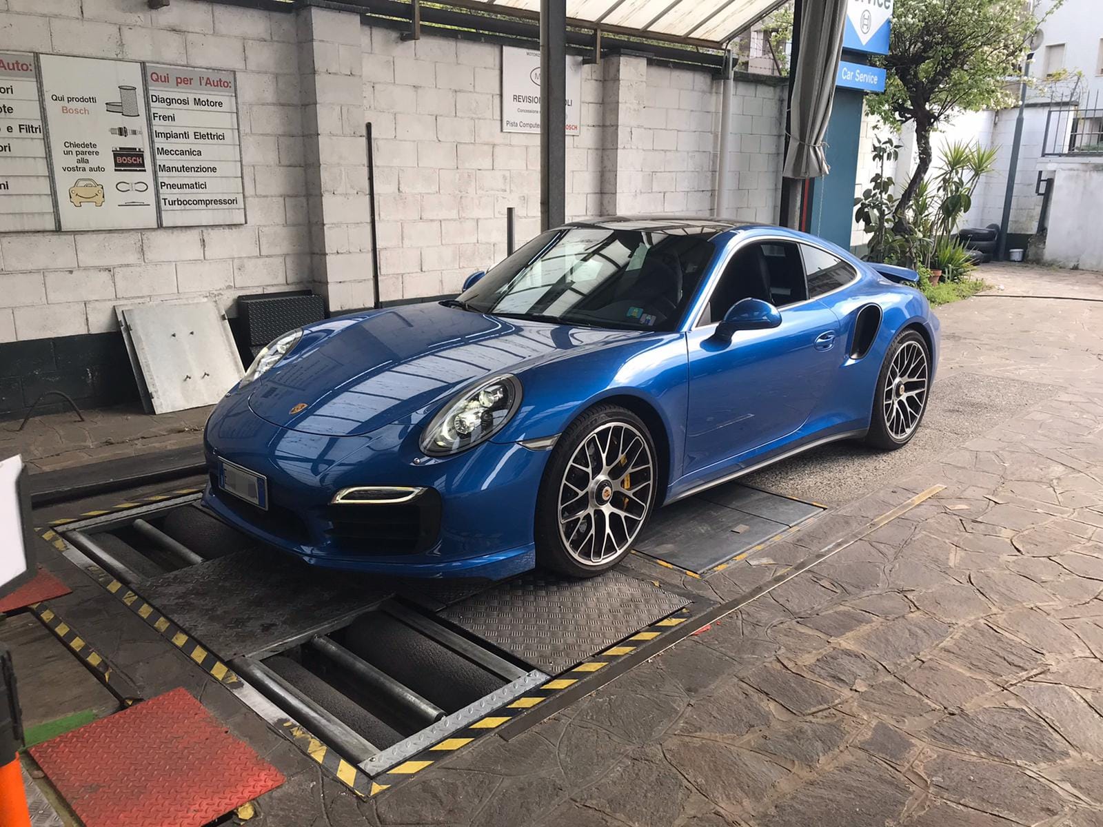 Un meccanico utilizza un tablet accanto al cofano aperto di un'auto in un'officina meccanica molto frequentata.