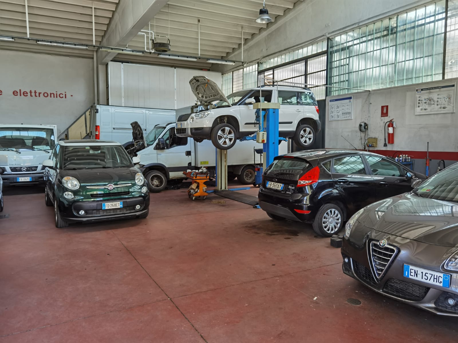 Auto in un'officina meccanica, una delle quali sollevata su un ponte, con i meccanici al lavoro al di sotto.