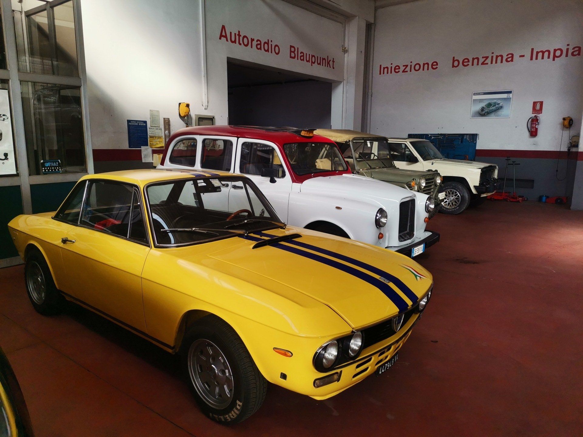 Berlina d'epoca classica di colore grigio chiaro esposta in un ambiente interno su un pavimento rosso.