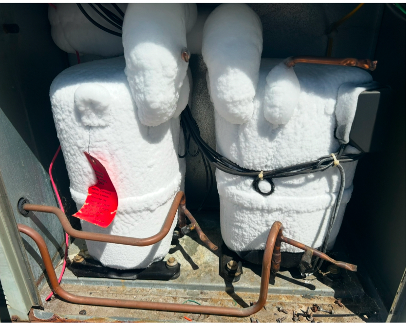 Two HVAC compressors inside a metal cabinet are covered in thick, white frost or ice.