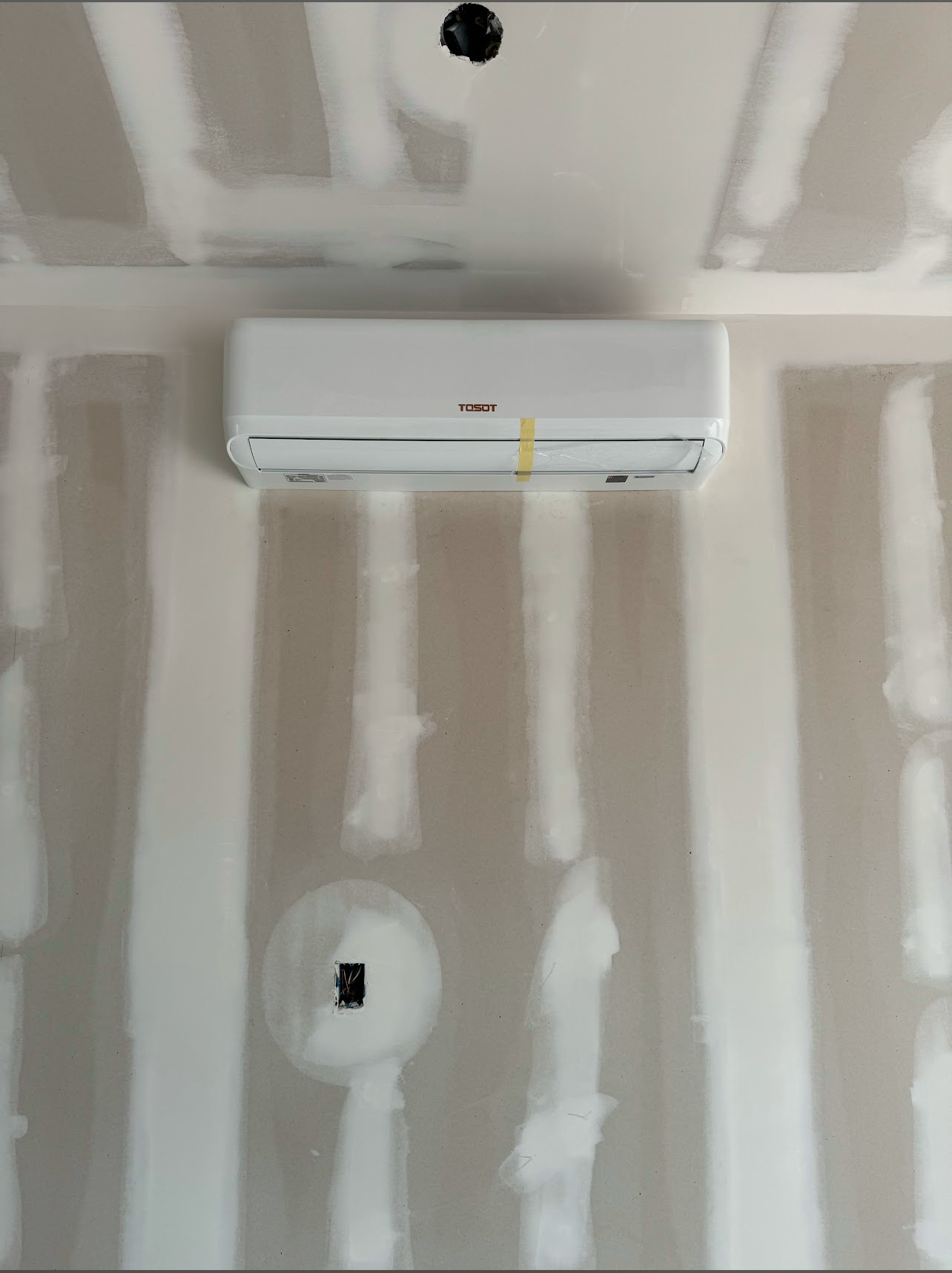 A white ductless mini-split air conditioner mounted on an unfinished drywall wall with visible seams and tape.
