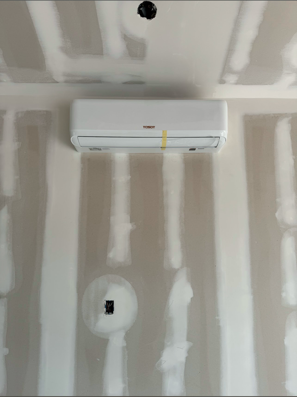 A white ductless mini-split air conditioner mounted on an unfinished drywall wall with visible seams and tape.
