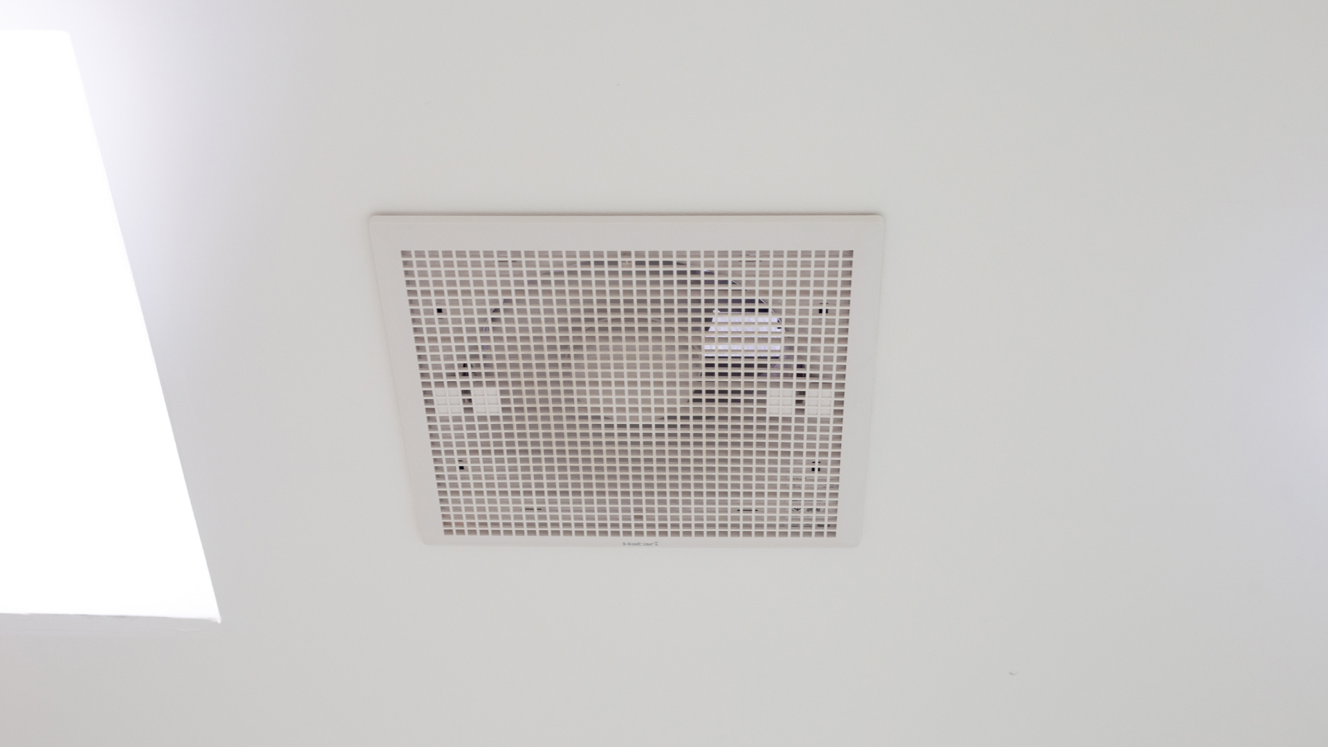 A square, white ventilation grille set flush into a smooth, white ceiling.