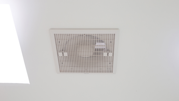 A square, white ventilation grille set flush into a smooth, white ceiling.