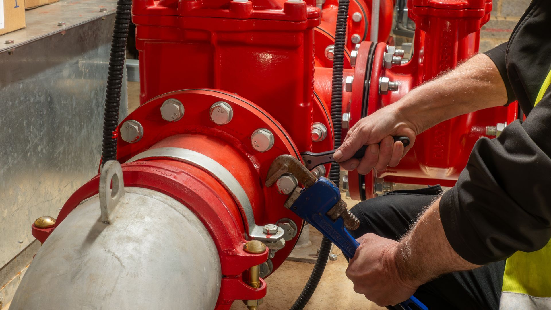 Technician tightening bolts on a large red industrial fire protection pipe system with wrenches.