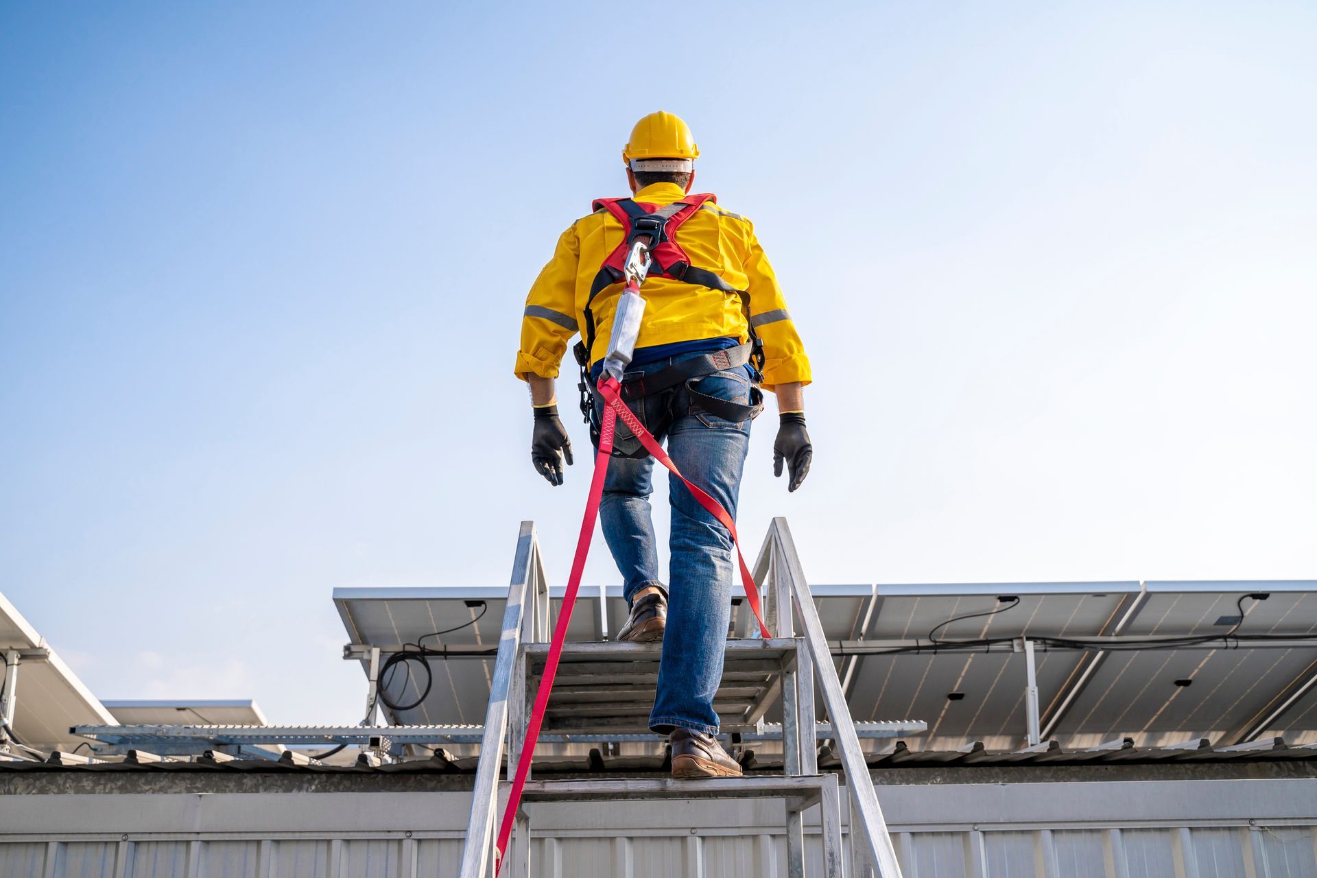 Worker in safety gear climbing a ladder to a rooftop.