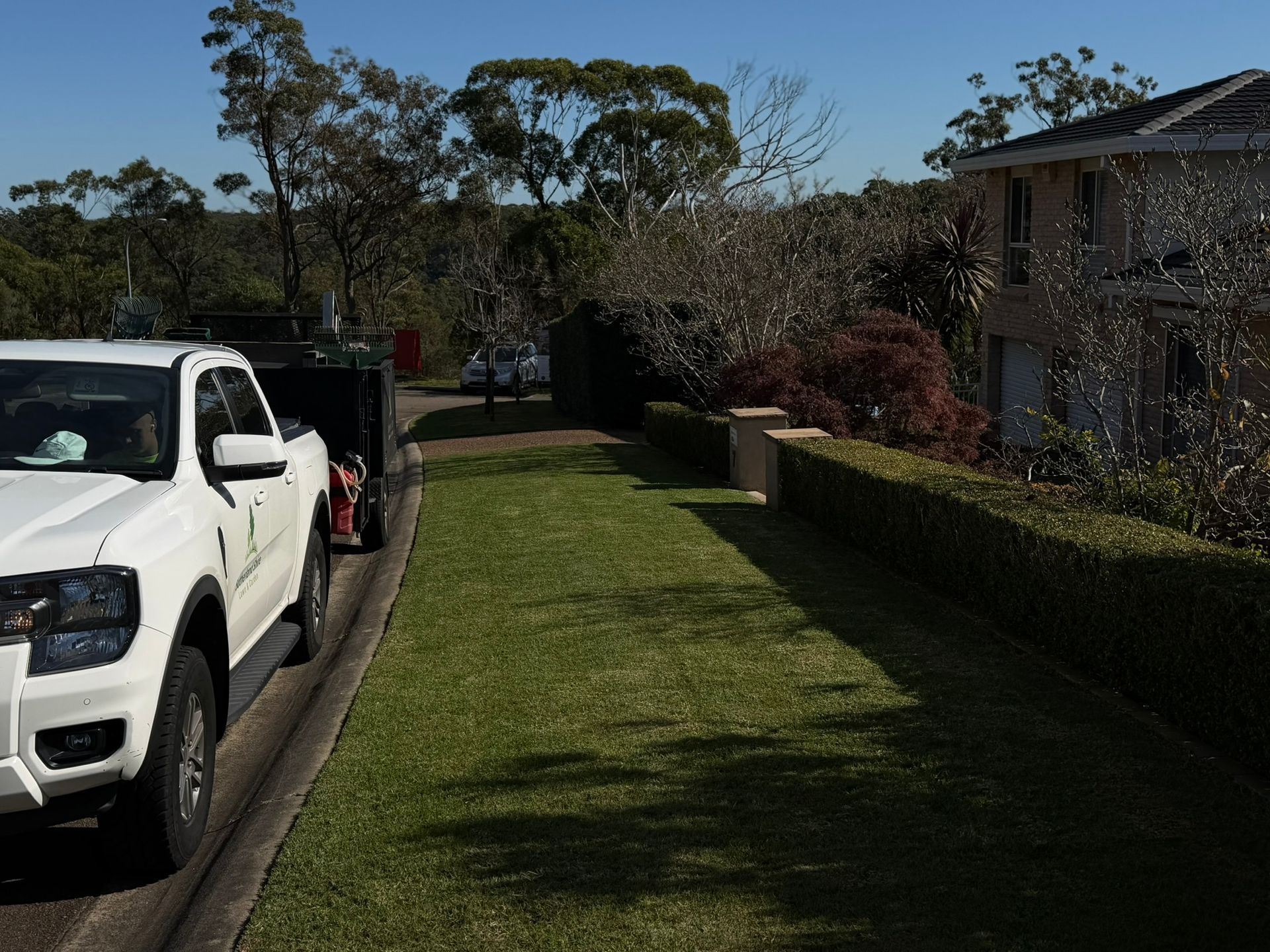 Driveway beside a white pickup truck, with a grassy lawn and hedge next to a brick apartment building.ivy