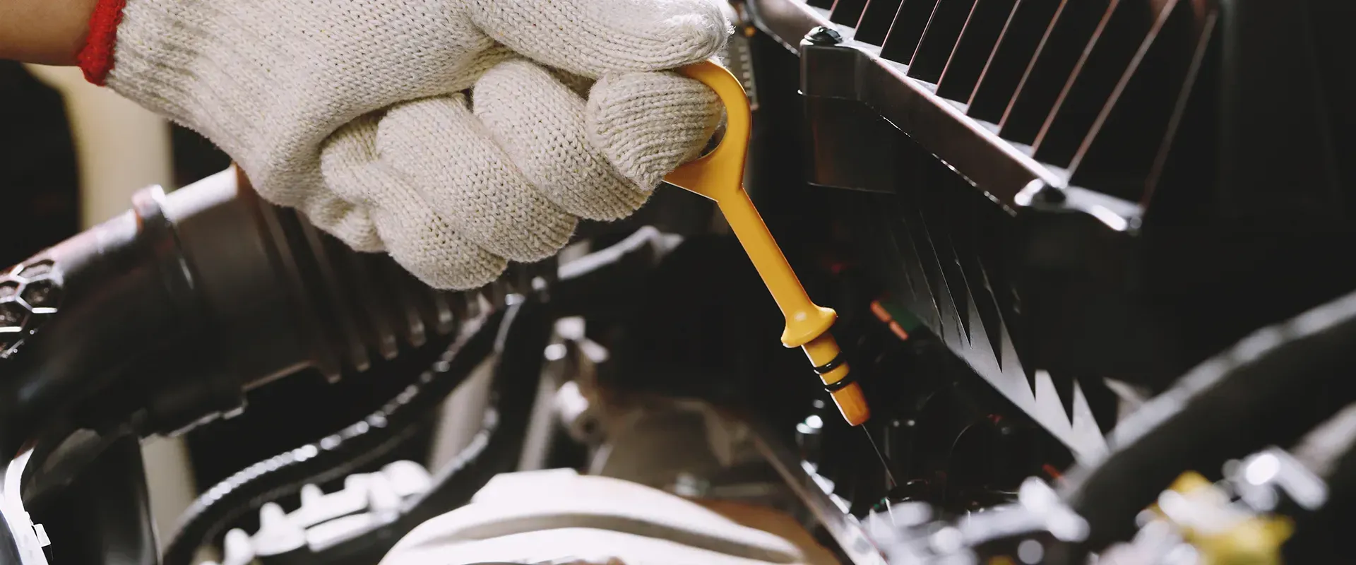 A gloved hand pulls out a yellow dipstick from an engine.