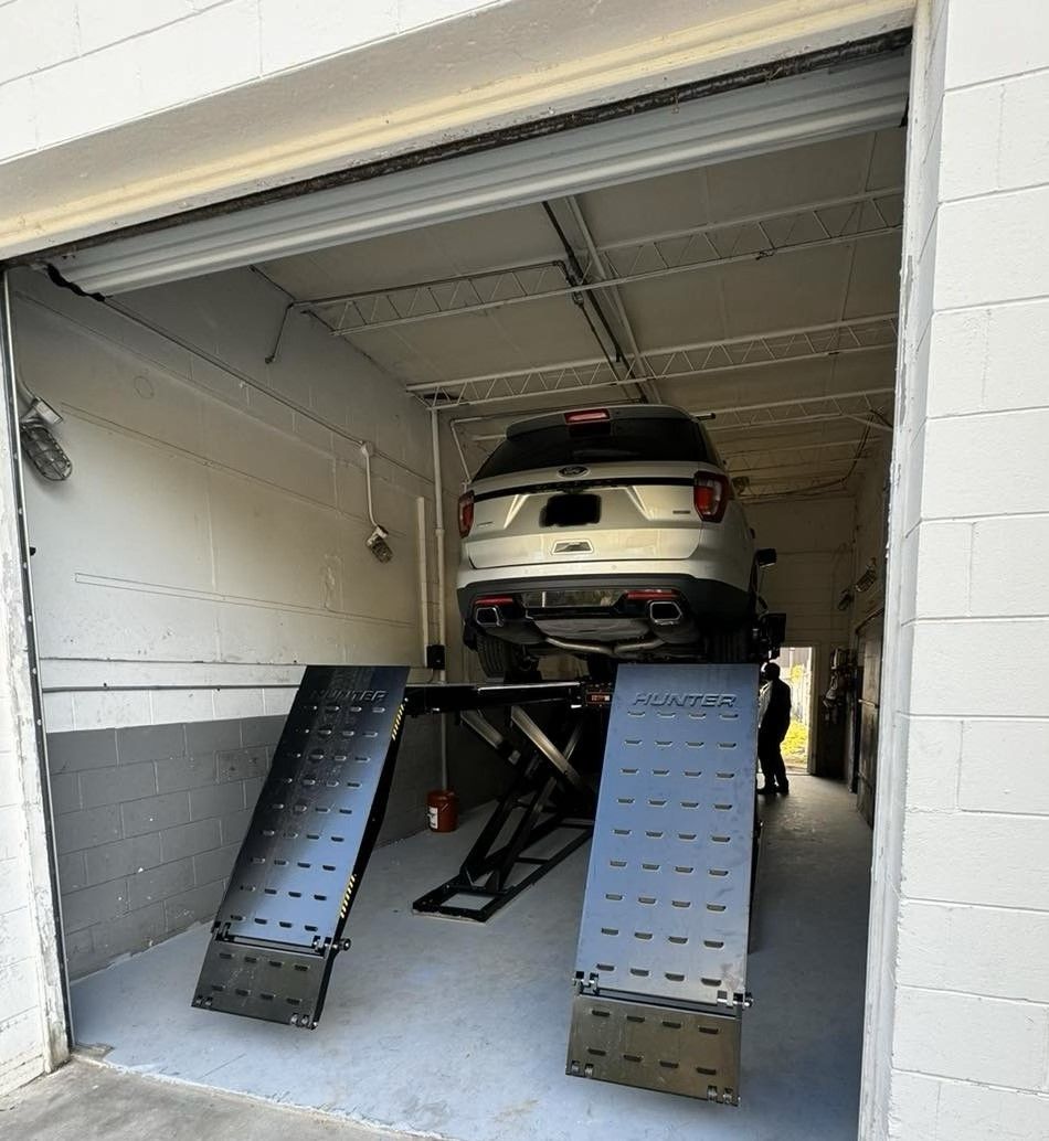 Silver SUV on a car lift inside a white garage with the door partially open.