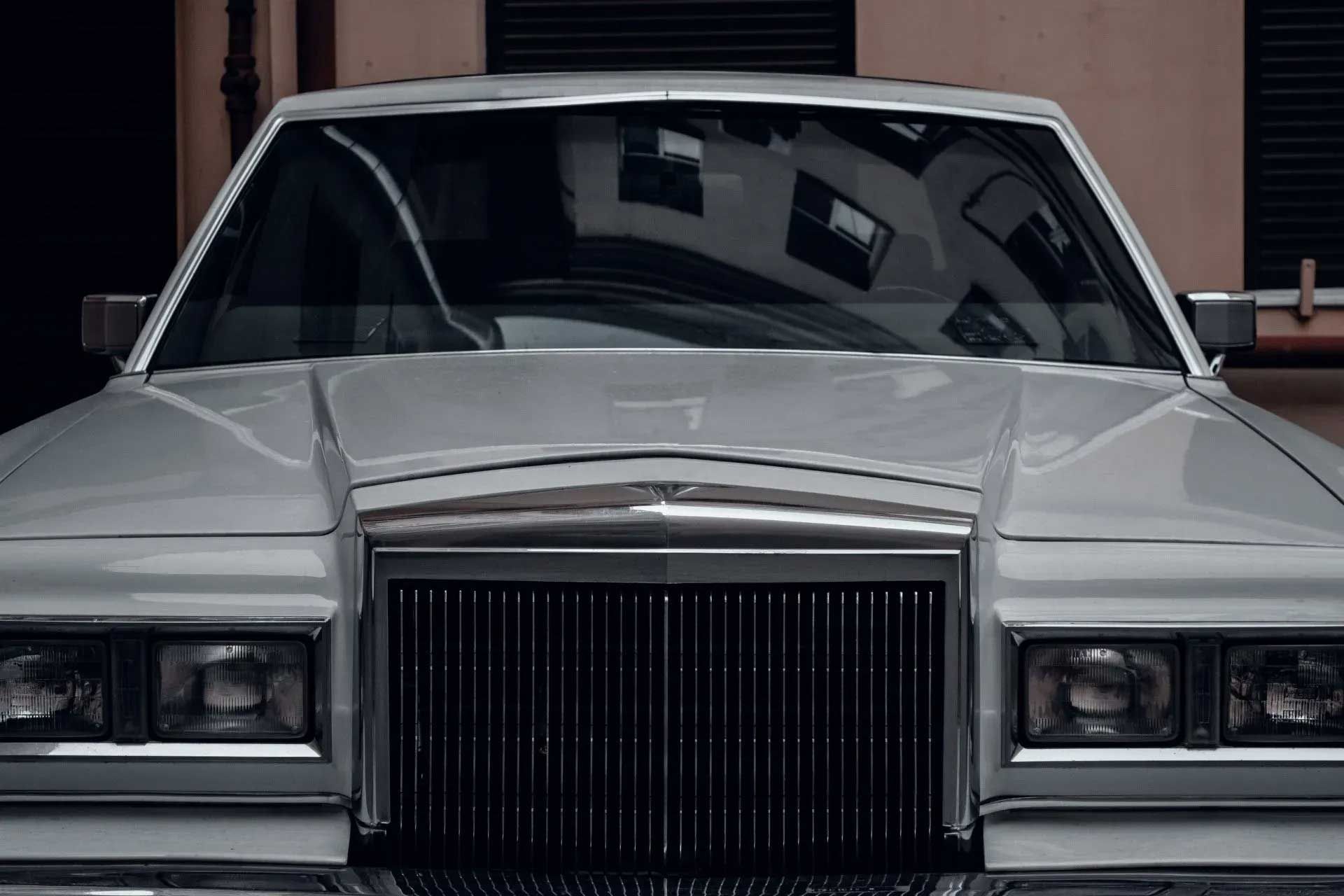 White vintage Lincoln sedan, front view, reflecting building in windshield.