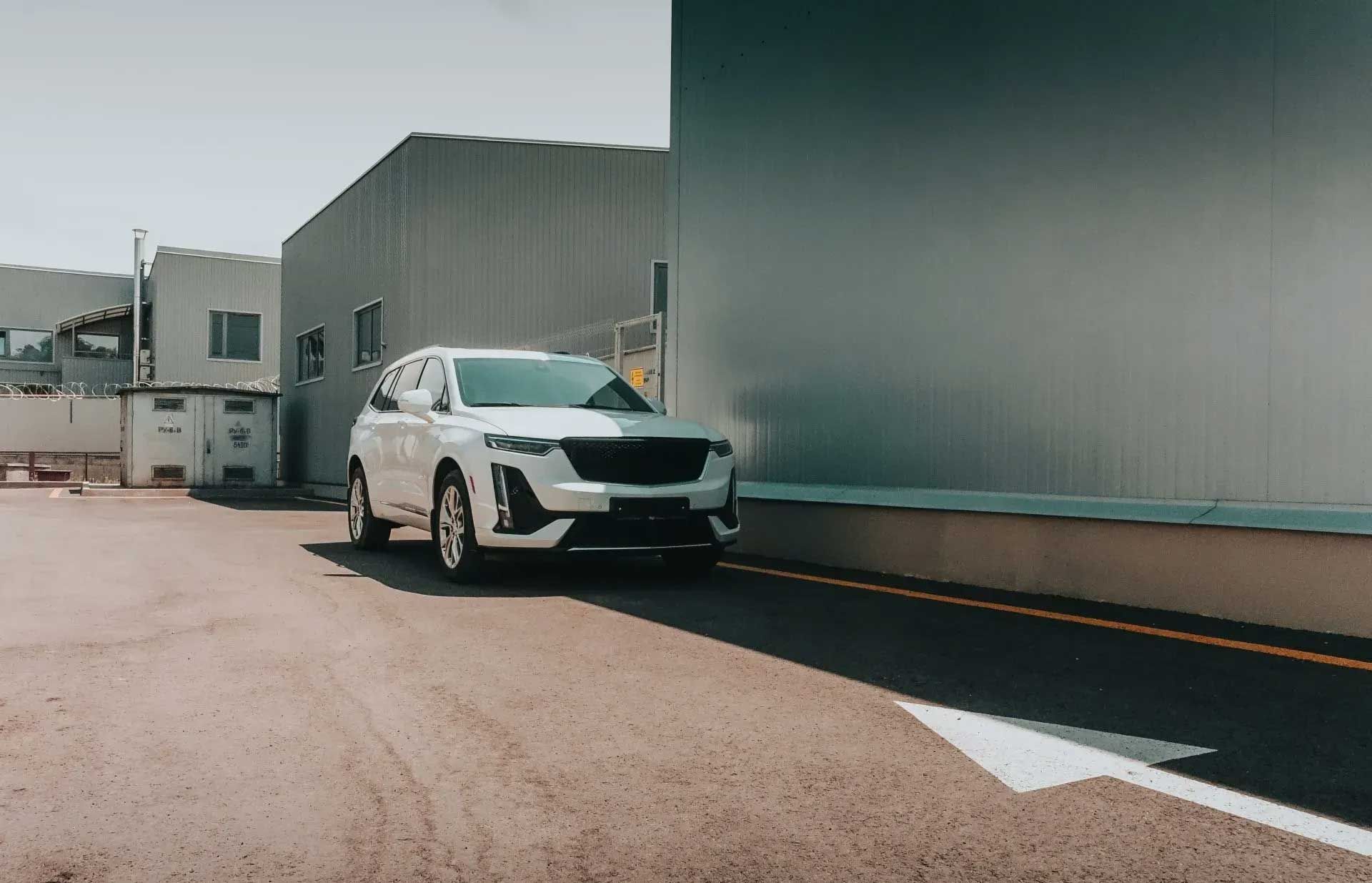 White SUV parked beside a gray industrial building. Arrow on pavement points right.
