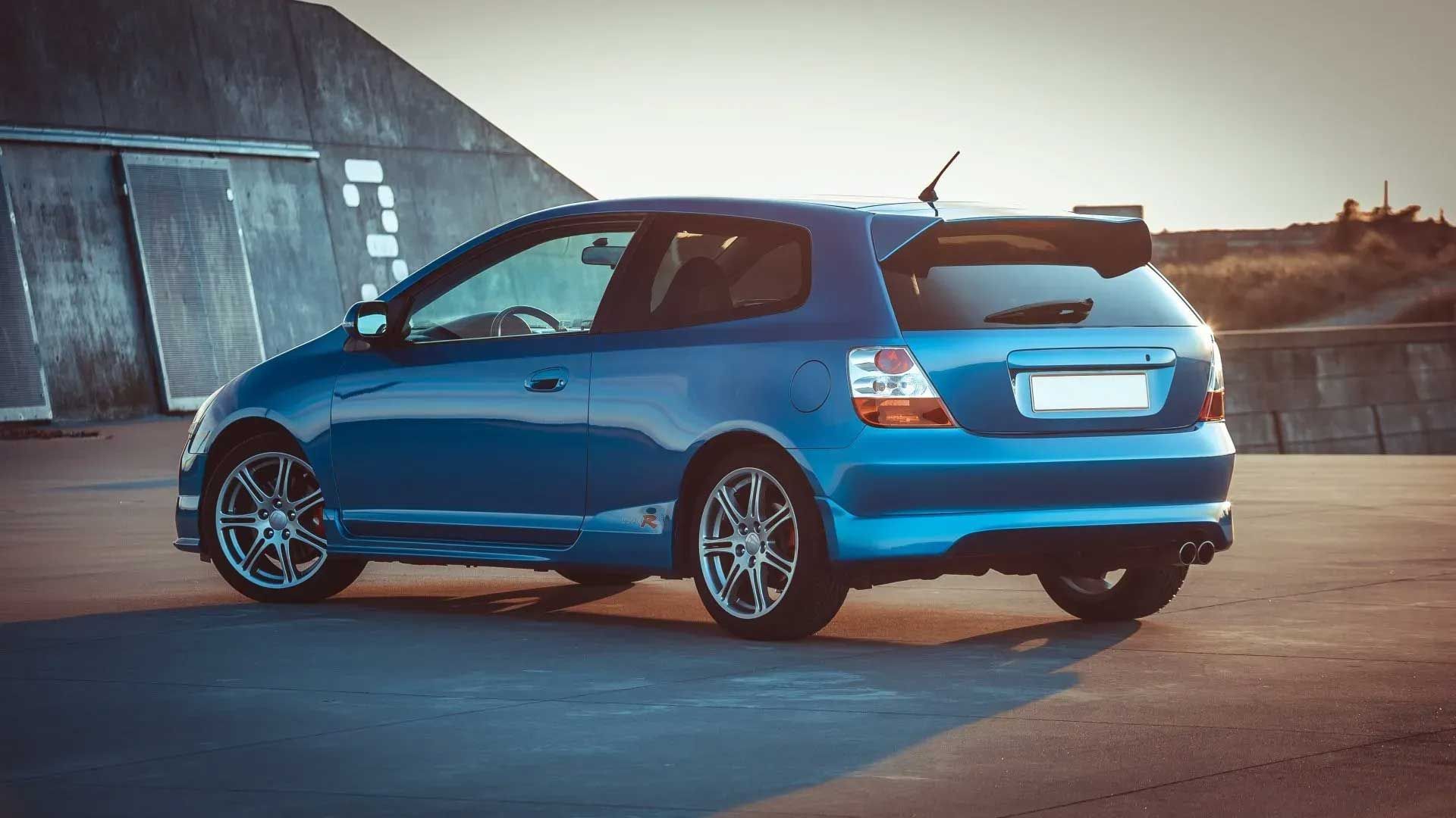 Blue Honda Civic hatchback parked outdoors, metallic wheels, spoiler.