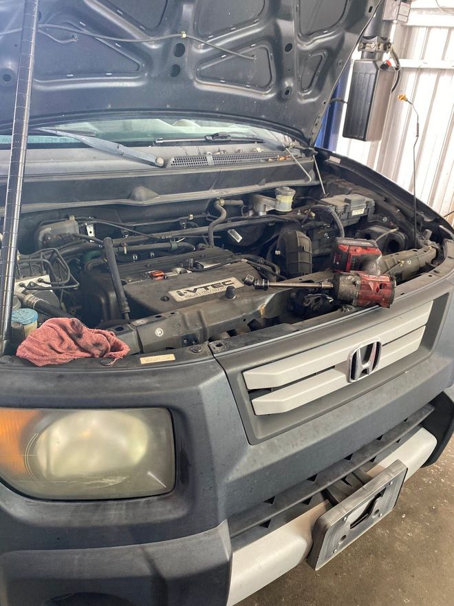 Honda Element with open hood at a garage, engine exposed, tool present, red cloth on the front.