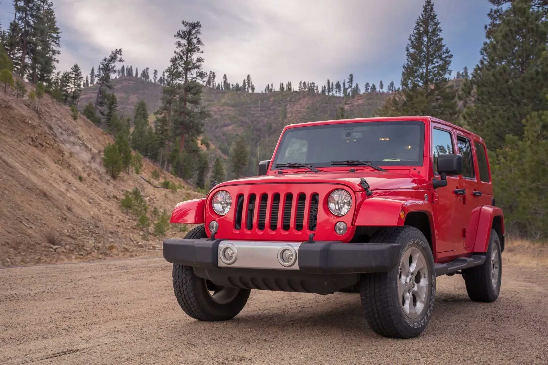Red Jeep parked on a dirt road in a mountainous, forested landscape.