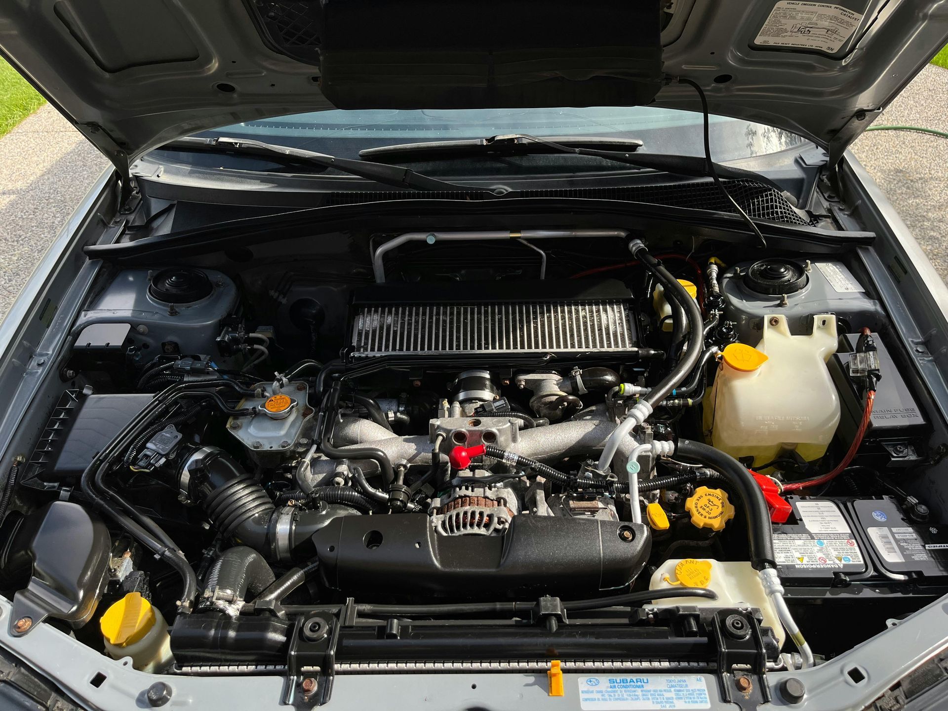 Gray Subaru engine bay with various components, including hoses, reservoir, and air filter.