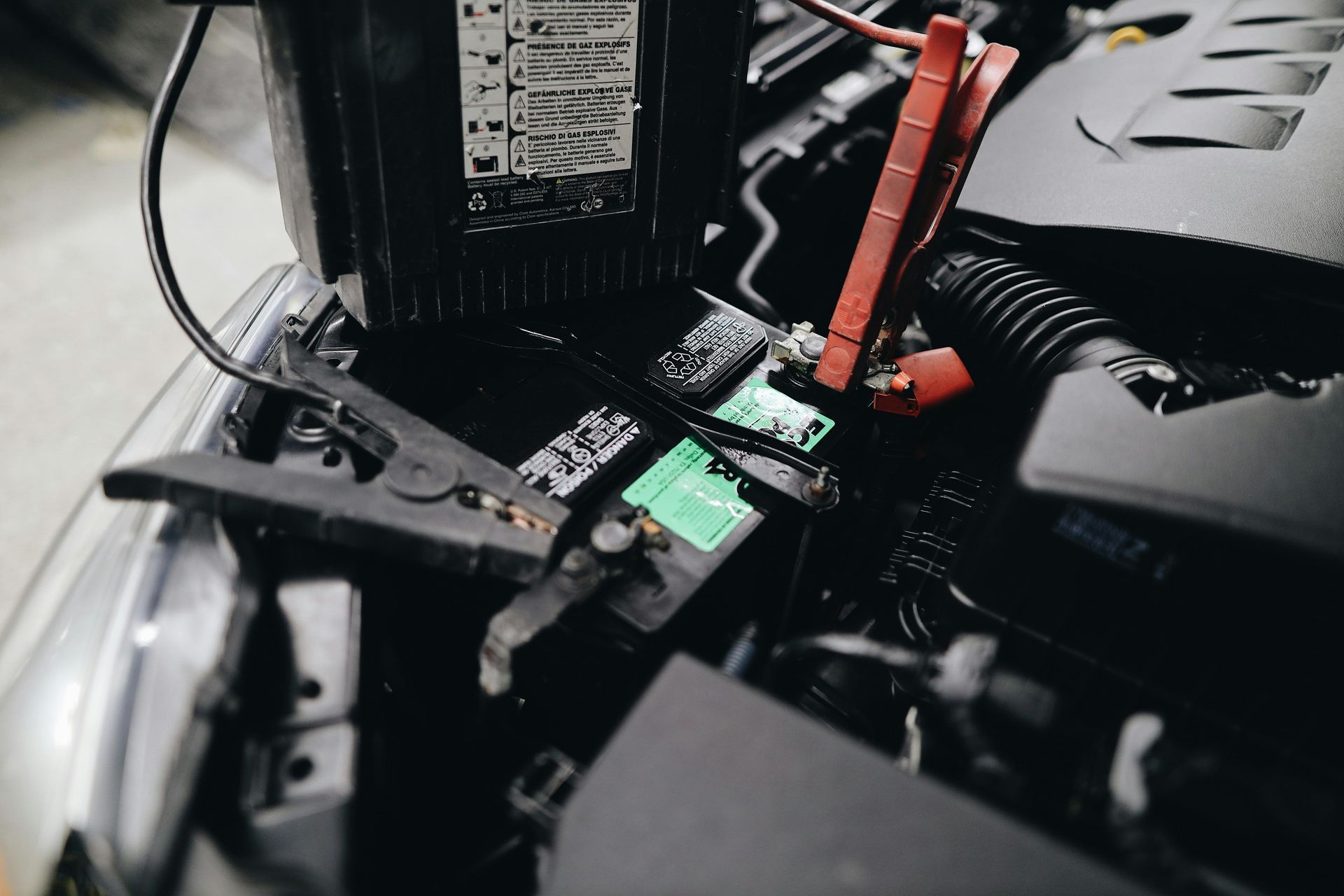 Car battery being jump-started; black clamps connected to battery terminals, red and black cables connected to another vehicle.