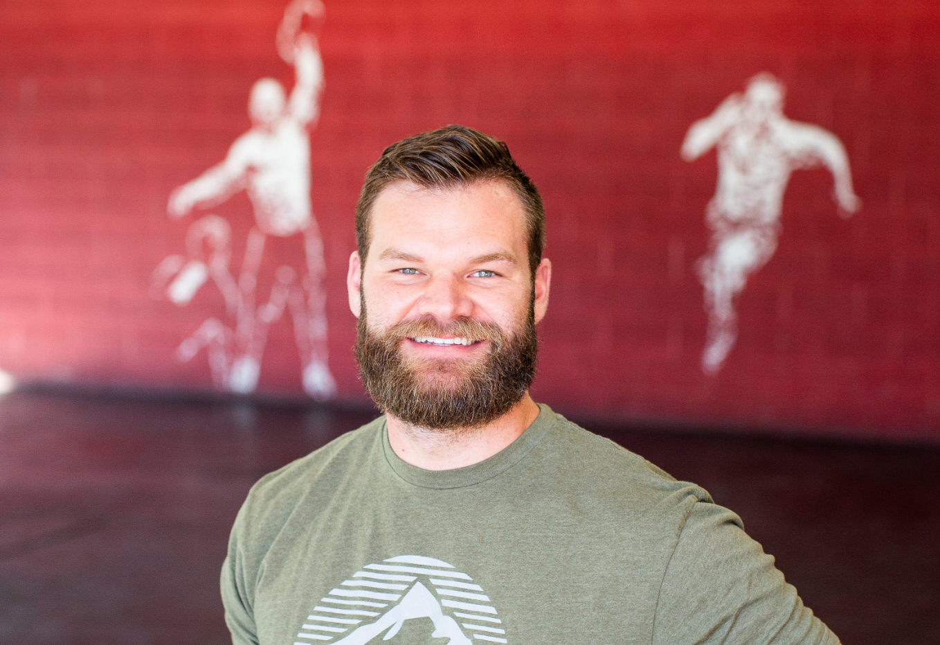 A man with a beard is smiling in front of a red wall.