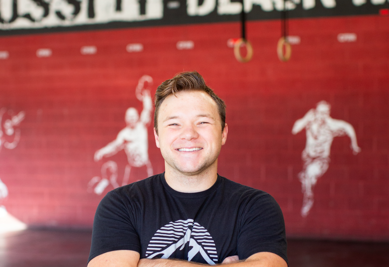 A man with down syndrome is smiling with his arms crossed in front of a red wall.