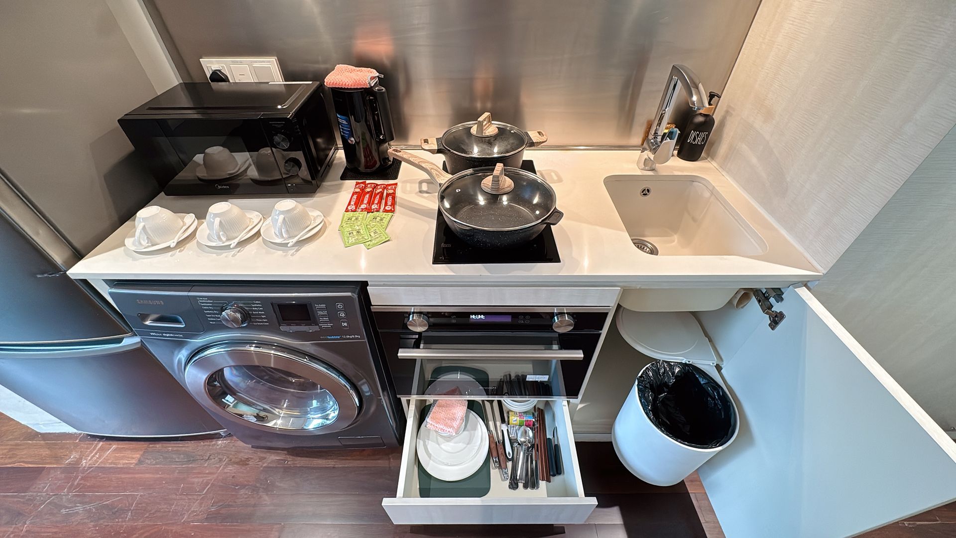 Small kitchen with appliances: washing machine, microwave, stove, sink, and open drawer with dishes.