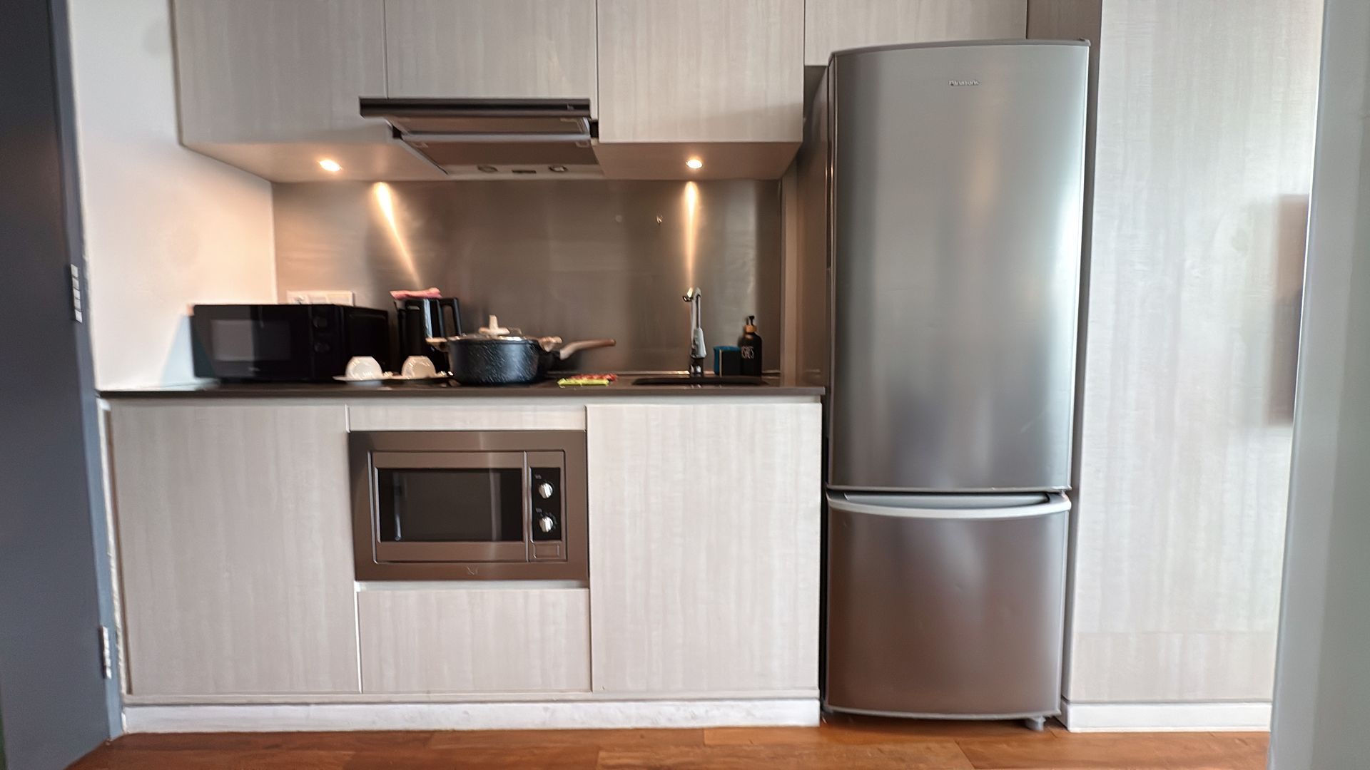 Small modern kitchen with light wood cabinets, stainless steel appliances, and a microwave.