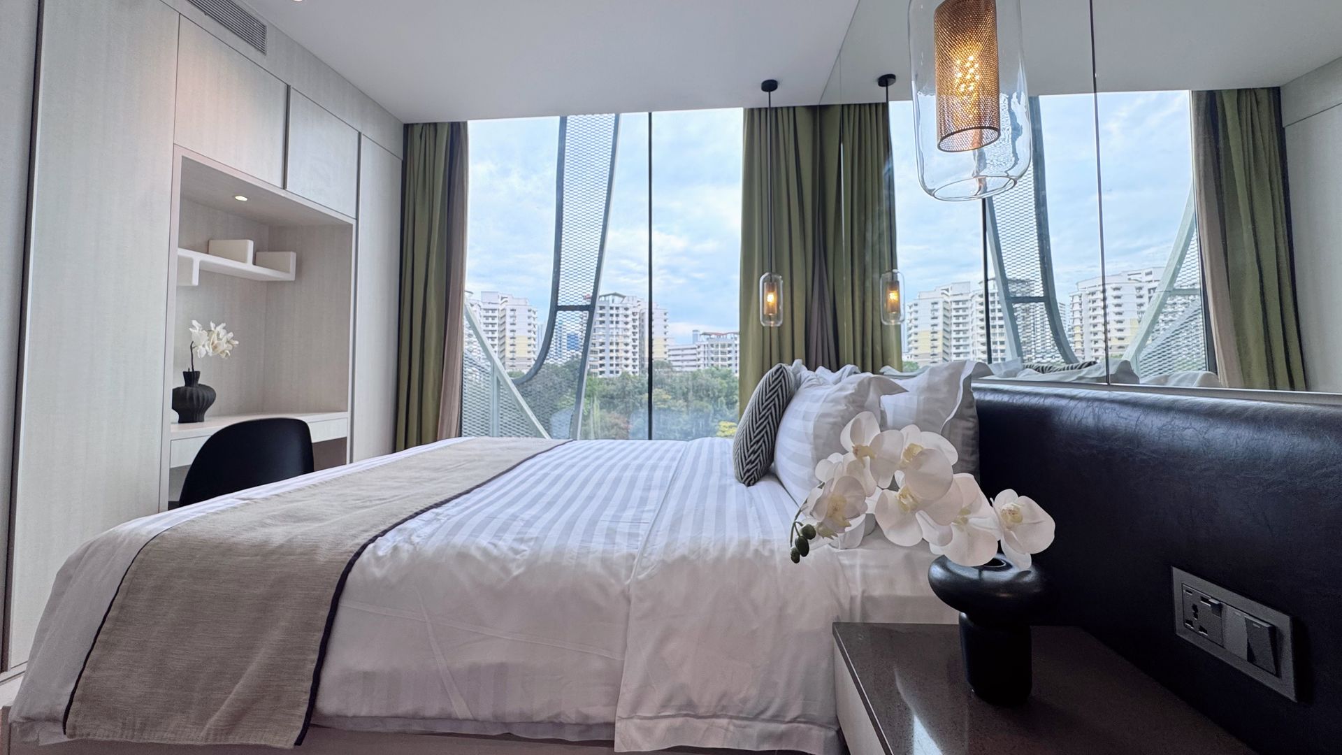 Hotel bedroom with large window, bed, desk, and city view.