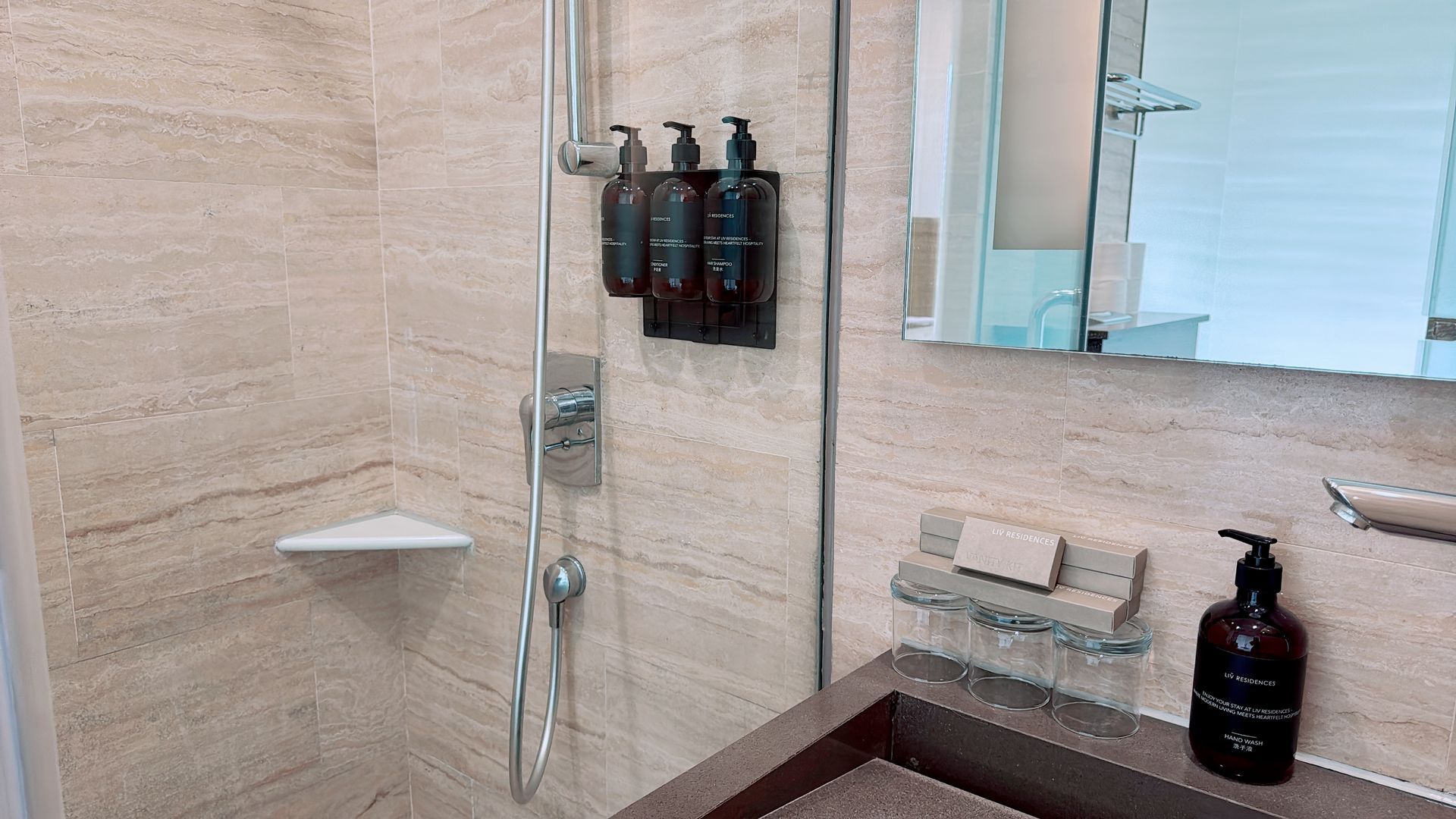 Bathroom with beige stone walls, shower, sink, soap, and toiletries.